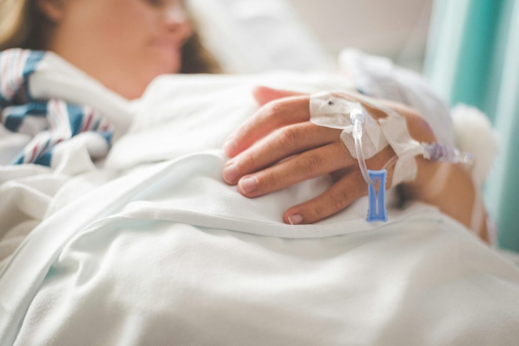 Eine Frau liegt mit einer Infusion in der Hand in einem Krankenhausbett.